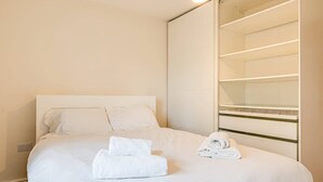 Hotellihuone, jossa on sänky, yöpöytä, peili ja vaatekaappi.