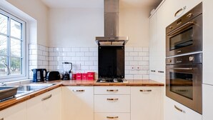Moderni keittiö, jossa on valkoiset kaapit, ruostumattomasta teräksestä valmistettu liesituuletin, kaksi uunia ja ikkuna, josta tulee luonnonvaloa.