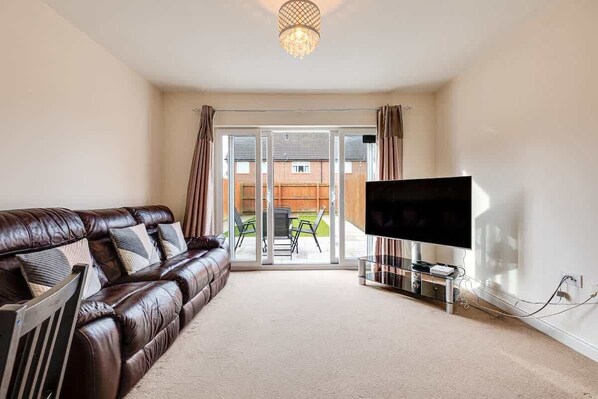 A living room with a leather sofa, a flat-screen TV, and a glass door leading to an outdoor area.