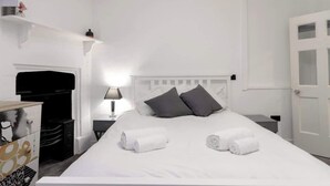 A hotel room with a white bed, grey pillows, a bedside table with a lamp, and a door with glass panels. - Chic Centrally Located 1Bed Apt in Chester (Chester)