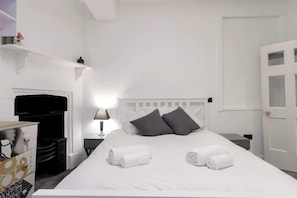 A hotel room with a white bed, grey pillows, a bedside table with a lamp, and a door with glass panels.