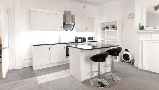 A modern kitchen with white cabinetry, a central island with bar stools, a built-in microwave, and a gas stove. - Chic Centrally Located 1Bed Apt in Chester (Chester)