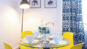 A dining area with a glass table, yellow chairs, white tableware, and a vase with white flowers. - Chic Centrally Located 1Bed Apt in Chester (Chester)