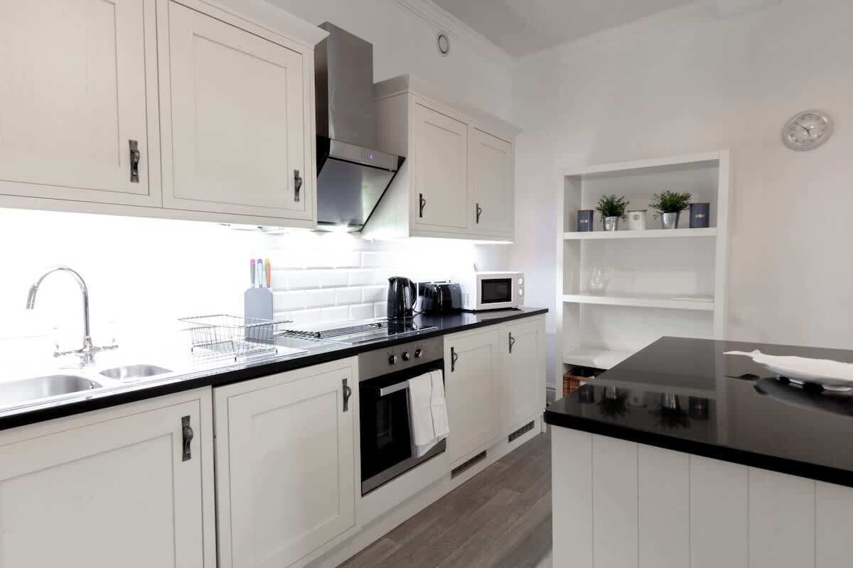 A modern kitchen with white cabinets, a black countertop, a stainless steel range hood, a microwave, and a sink.