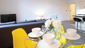 A modern living room with a sofa, a dining table set with white dishes and glasses, and a TV in the background. - Chic Centrally Located 1Bed Apt in Chester (Chester)