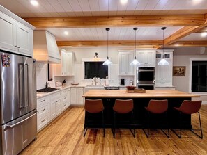 Een moderne keuken met witte kasten, een houten kookeiland met barstoelen, roestvrijstalen apparatuur en hangende lampen.