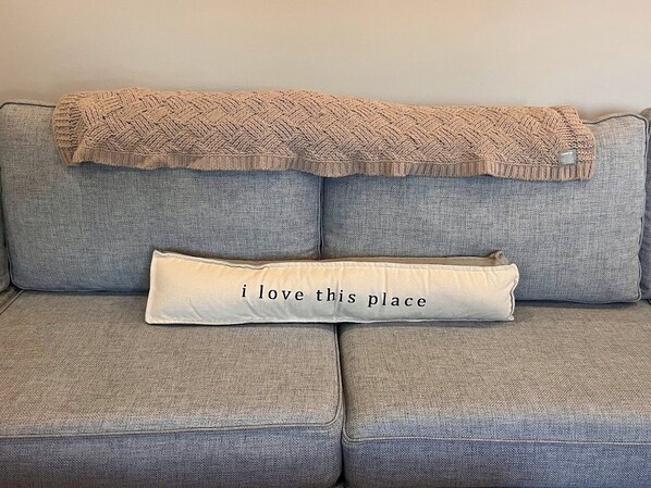 A grey sofa with a knitted throw blanket and a pillow with the text "I love this place".