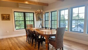 Comedor con mesa y sillas de madera, ventanas amplias y una araña.