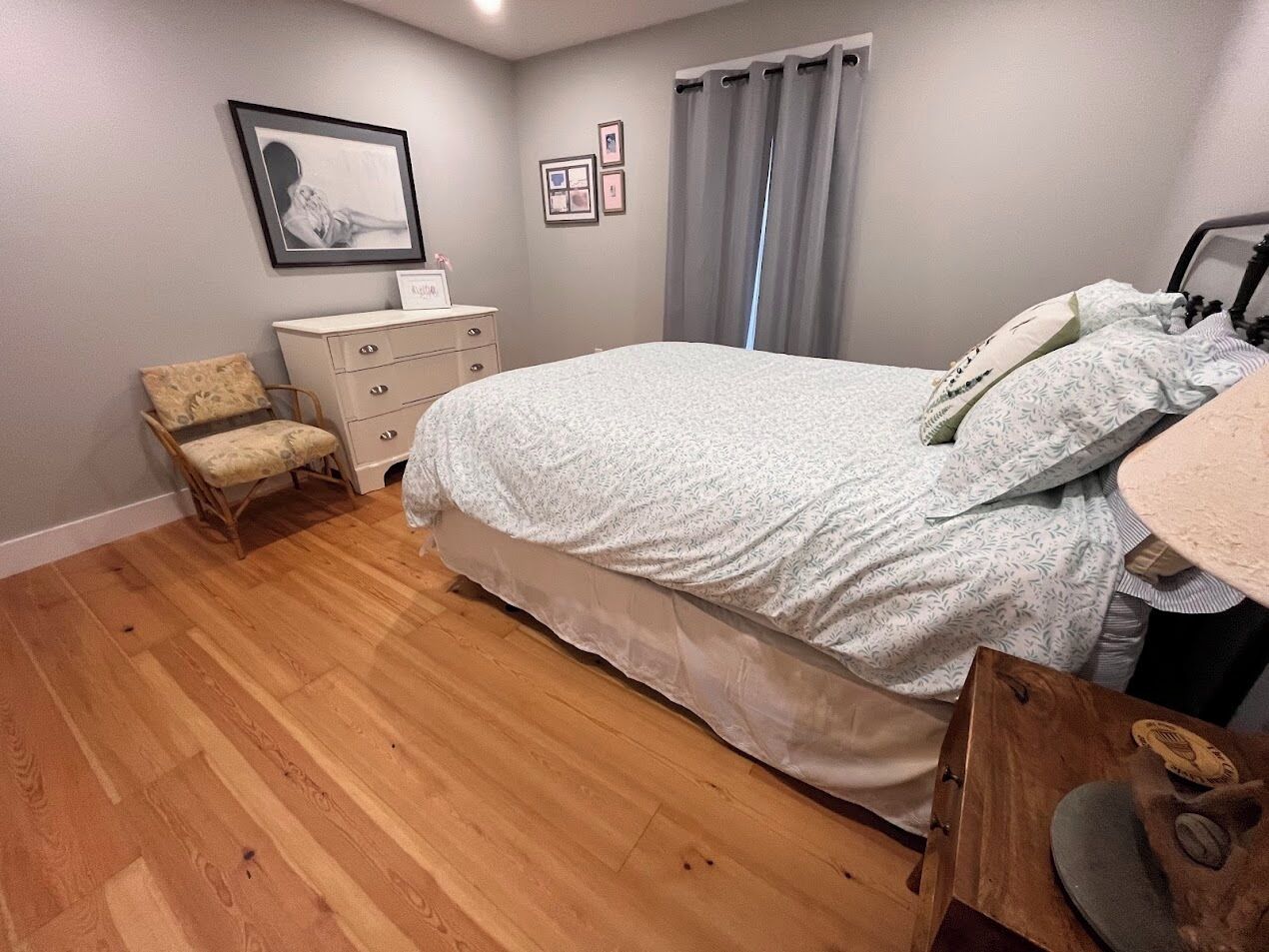 A bedroom with a large bed, a dresser, a chair, and a wooden nightstand.