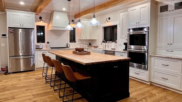 Una cocina moderna con una isla central, taburetes de bar, electrodomésticos de acero inoxidable e iluminación colgante.