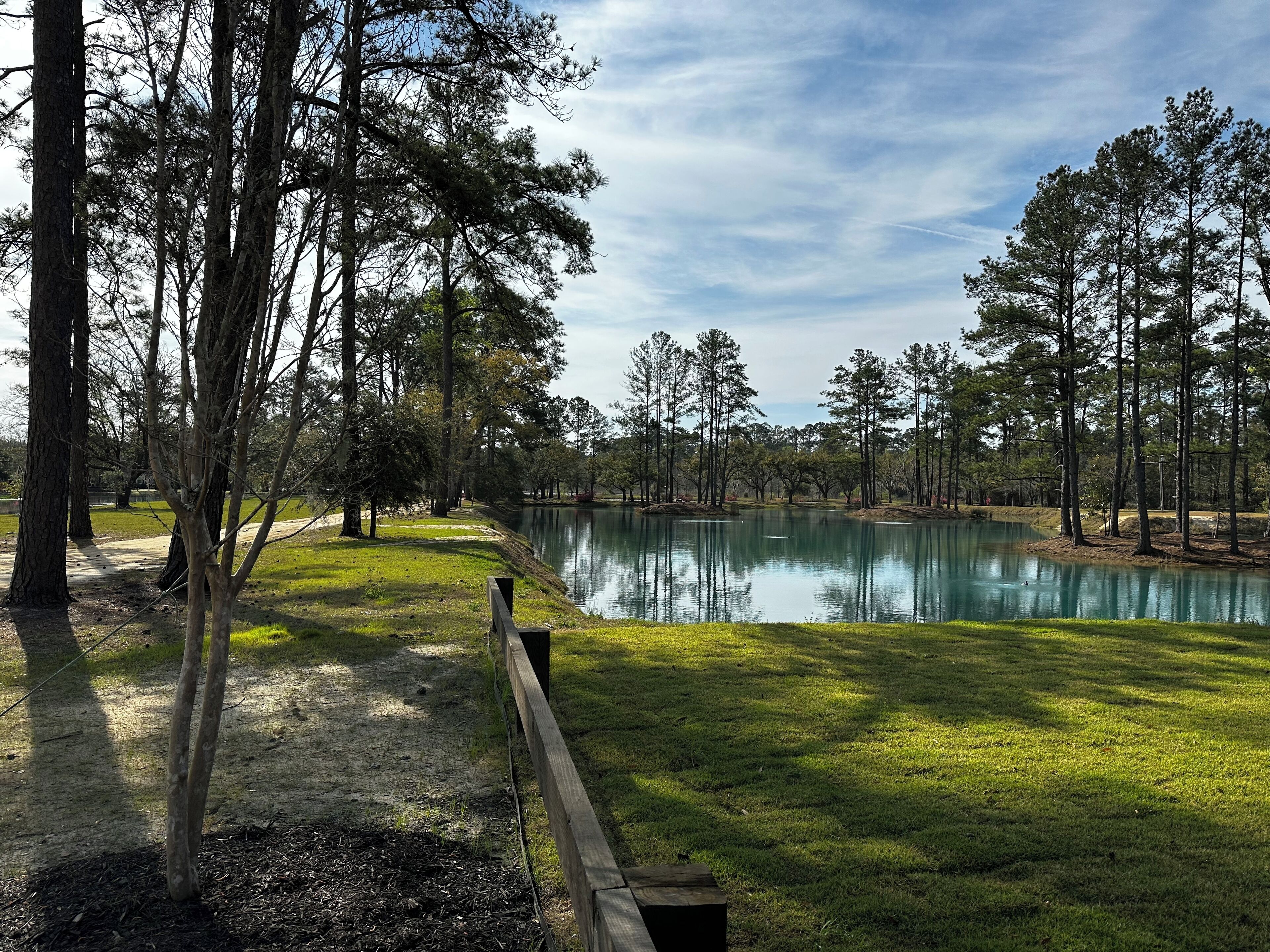 A serene lakeside view with a wooden fence, trees, and a clear sky.