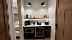 Un pasillo estrecho que lleva a una cocina pequeña con microondas, cafetera y una barra para café.