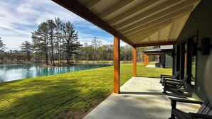 Un patio techado con mobiliario exterior, vista a un lago y zona verde con árboles.