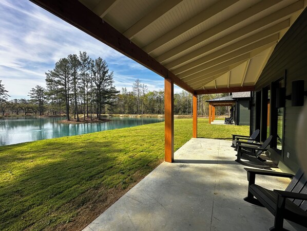 A covered patio with outdoor seating, a view of a lake, and a grassy area with trees.