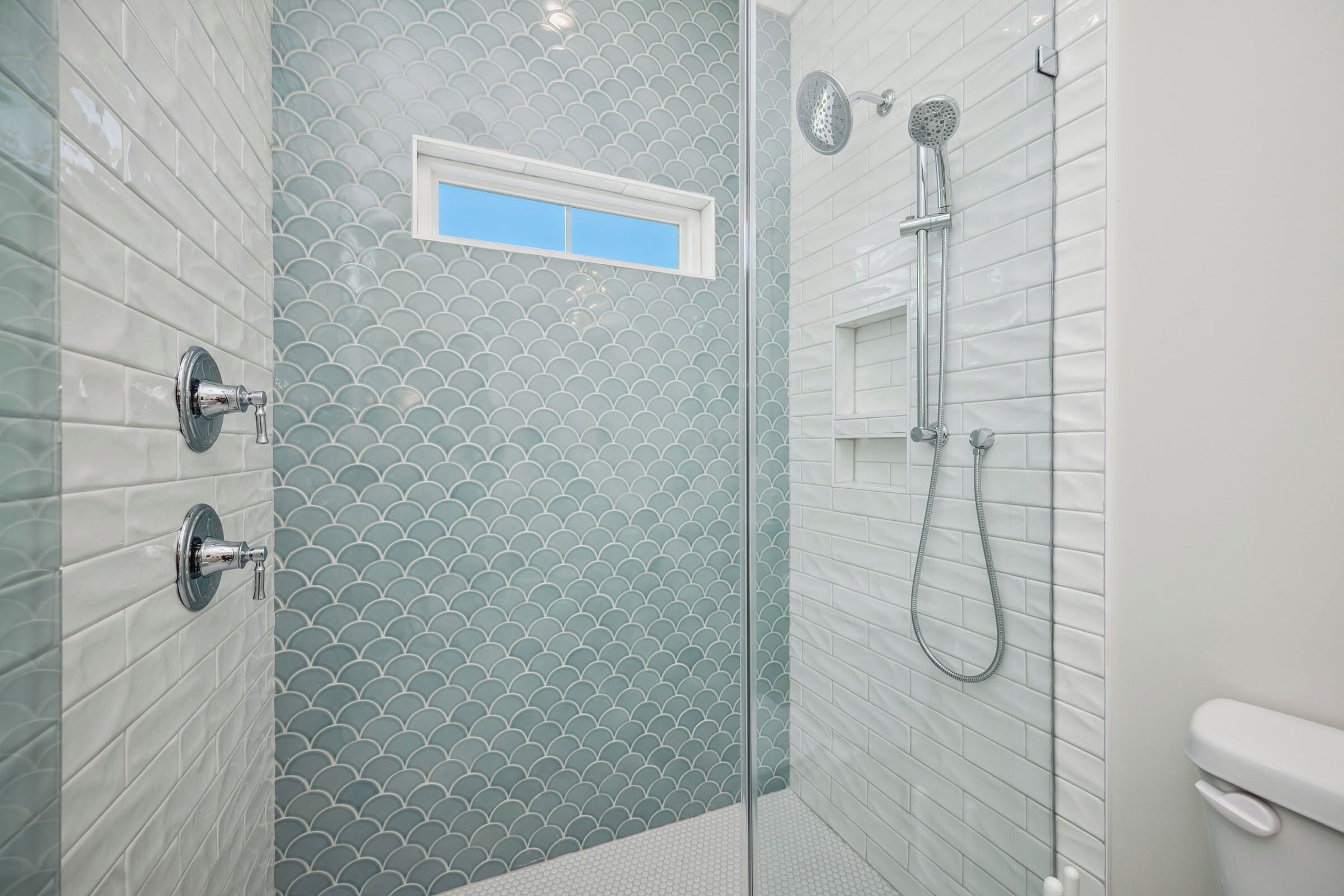 A shower with a glass door, a handheld showerhead, and a wall-mounted faucet.