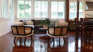 Un salon spacieux doté d’un plancher en bois, de deux fauteuils en osier, d’un canapé et d’un coin repas avec une table et des chaises.