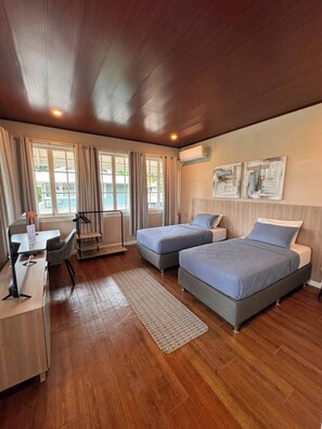 Une chambre d’hôtel avec deux lits, un bureau, une chaise et une fenêtre avec des rideaux.