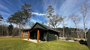 Ein modernes, offenes Pavillon mit dunklem Dach und Holzsäulen, umgeben von einem gepflegten Rasen und hohen Bäumen.