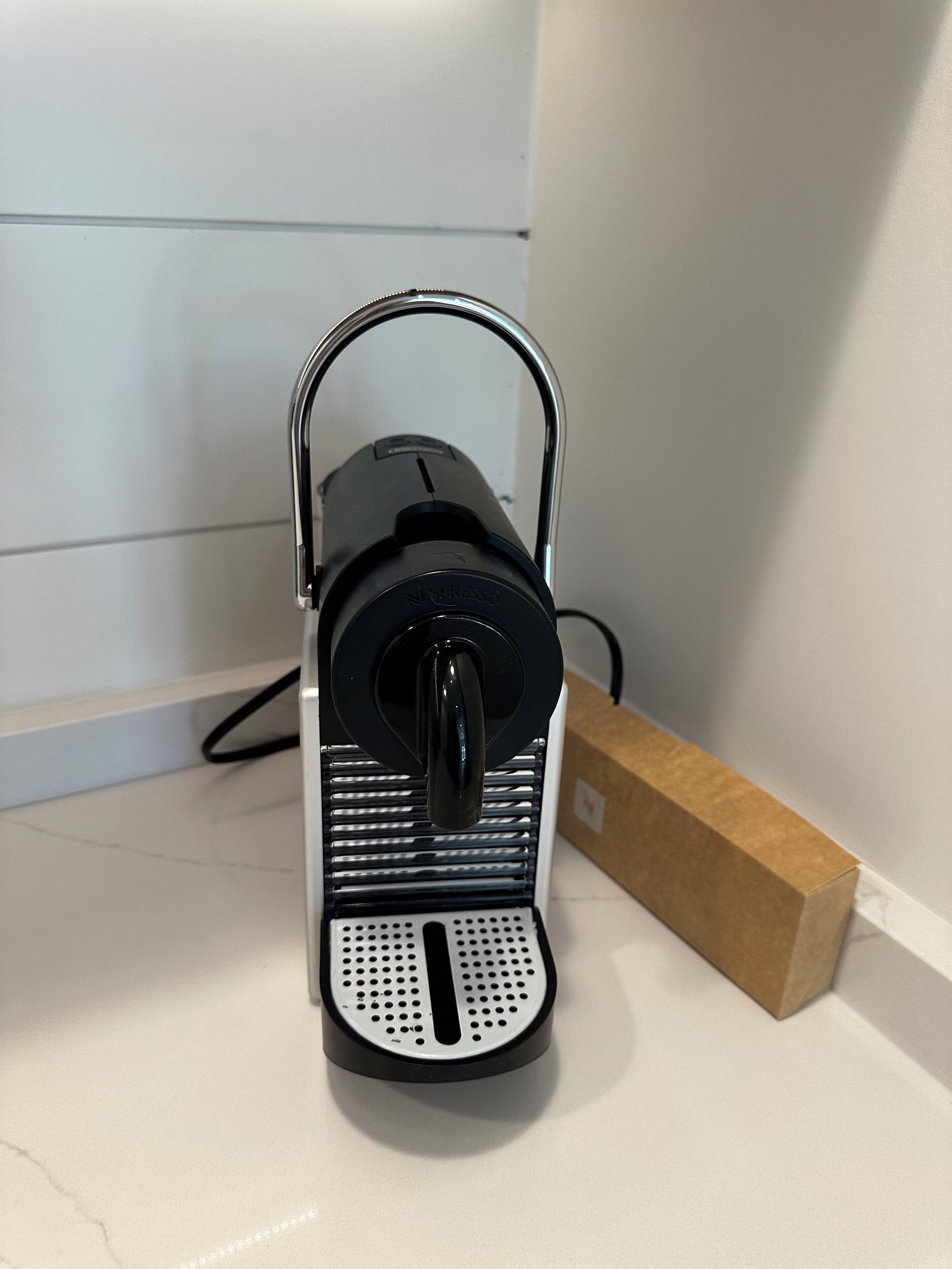 A black coffee maker on a white countertop with a cardboard box nearby.