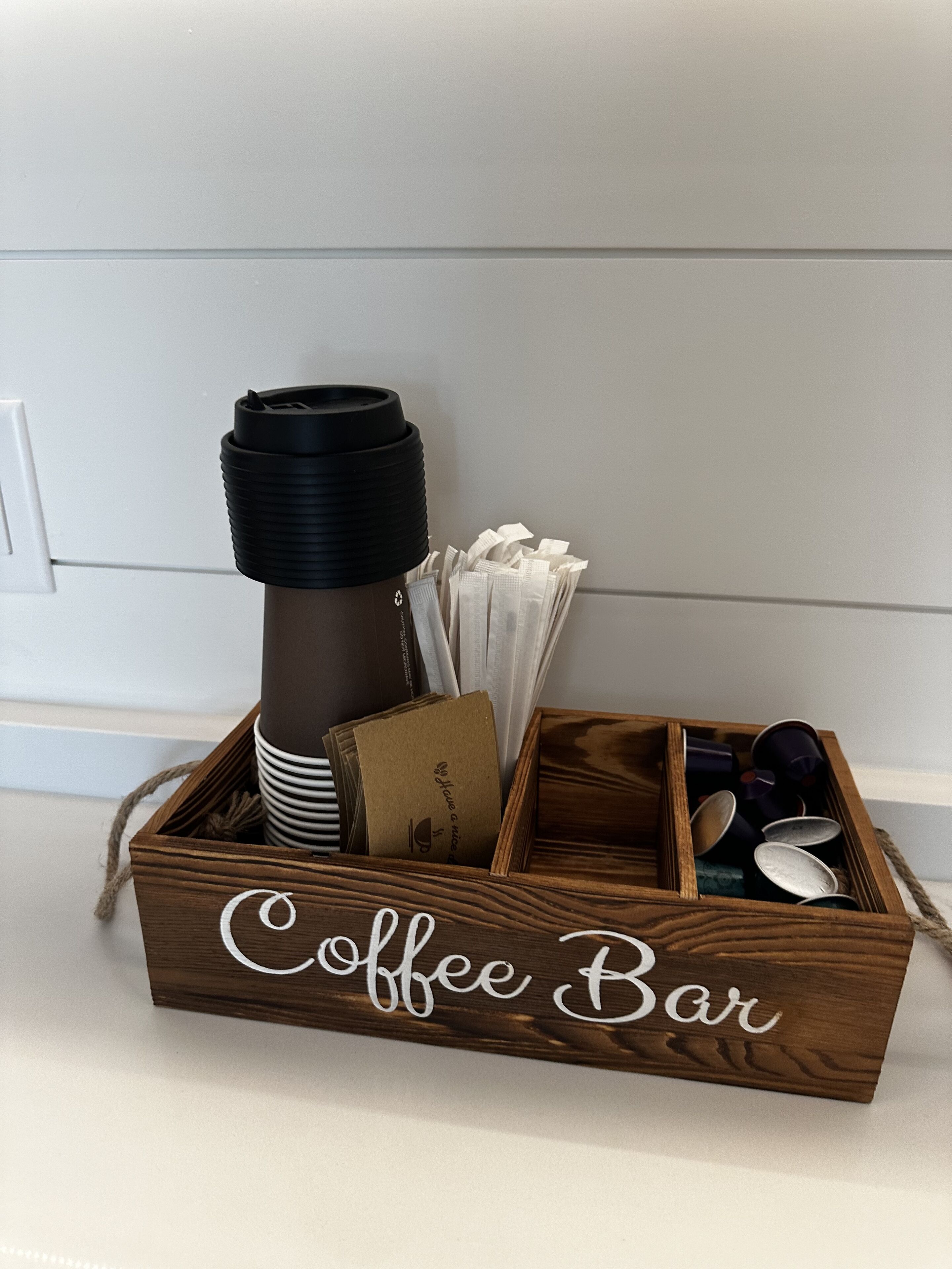 A wooden box labeled "Coffee Bar" containing a coffee maker, napkins, a card, and a cup.