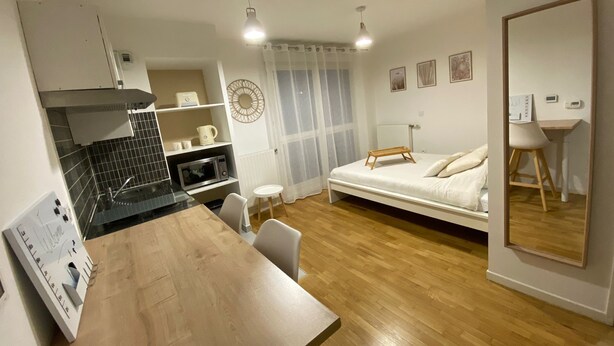 Una habitación compacta con kitchenette, una cama, una mesita y un espejo.