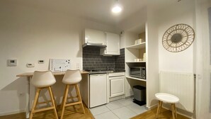Una cocina compacta con armarios blancos, un salpicadero de baldosas negras, horno empotrado y una pequeña mesa blanca con dos taburetes.