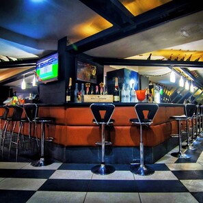 A bar area with a checkered floor, a counter with bottles, and a TV screen. - Laroy Suites (Abeokuta)