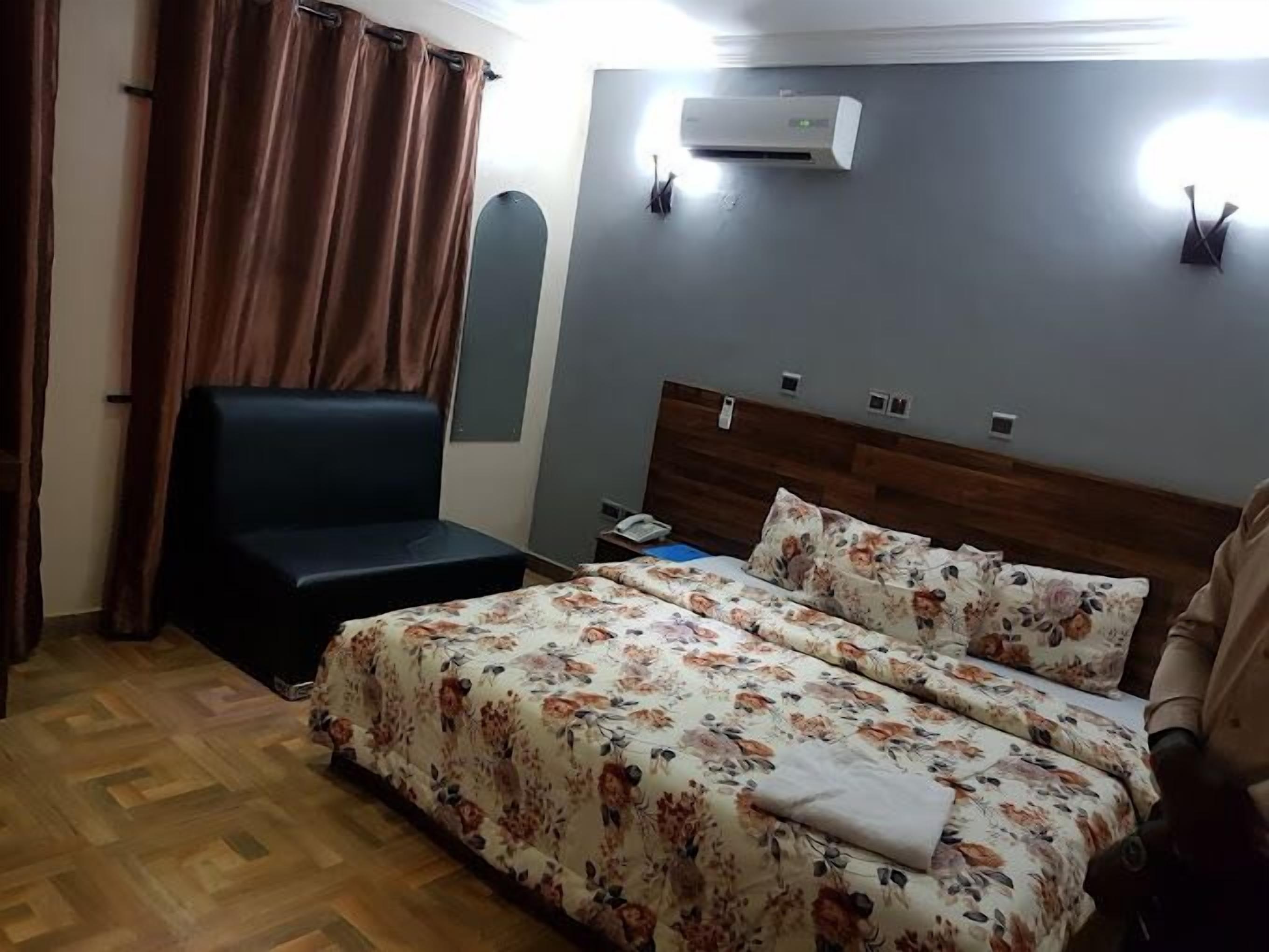 A hotel room with a bed, a small desk, a chair, an air conditioning unit, and a curtain.