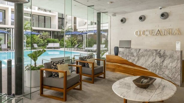 Un hall d’hôtel moderne avec vue sur la piscine, un espace salon et un comptoir d’accueil.