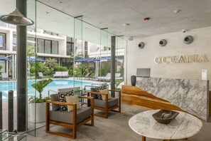 A modern hotel lobby with a pool view, seating area, and a reception desk.