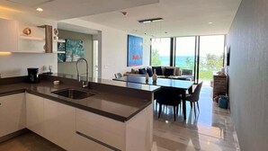 Une cuisine moderne dotée d’un îlot central, d’un coin repas avec une table et des chaises, et d’une grande fenêtre offrant une vue sur l’extérieur.