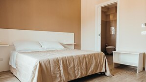 A bedroom with a bed, bedside tables, a door leading to a bathroom, and a white bench. - AFFITTACAMERE MIRA SINNI  (Episcopia)