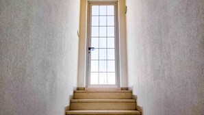 Un escalier étroit mène à une porte dont le vitrage est orné d’un motif quadrillé.