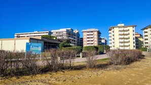 Un hôtel à plusieurs étages, une enseigne et une zone sablonneuse à la végétation clairsemée.