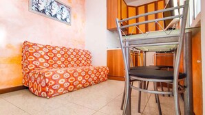 Une petite pièce comprenant un canapé, une chaise en métal et un coin cuisine.