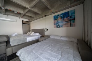 A hotel room with two beds, a sofa, a ceiling with exposed beams, and a modern abstract painting on the wall. - Epic Suites x Ahead (Pereira)