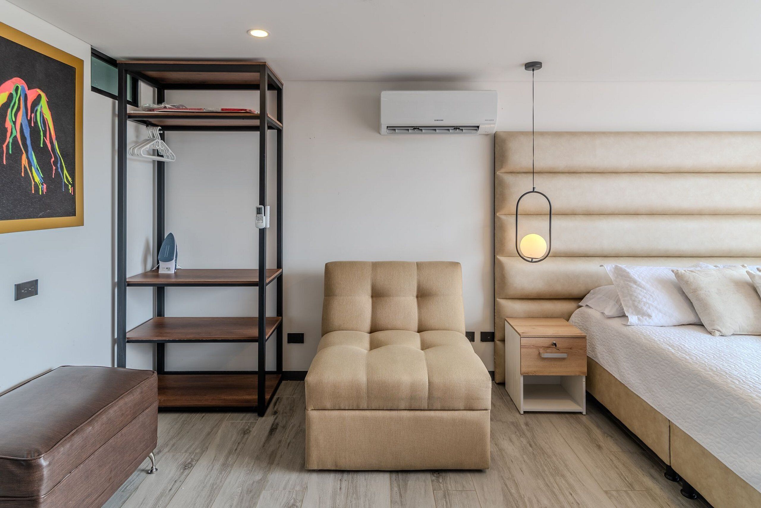 A modern bedroom with a sofa, a bed, a nightstand, a wardrobe, and an air conditioning unit.