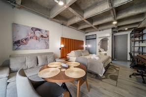 Ein moderner, gut beleuchteter Raum mit einer Couch, einem Bett, einem Esstisch mit Platzsets und einem großen abstrakten Gemälde an der Wand.