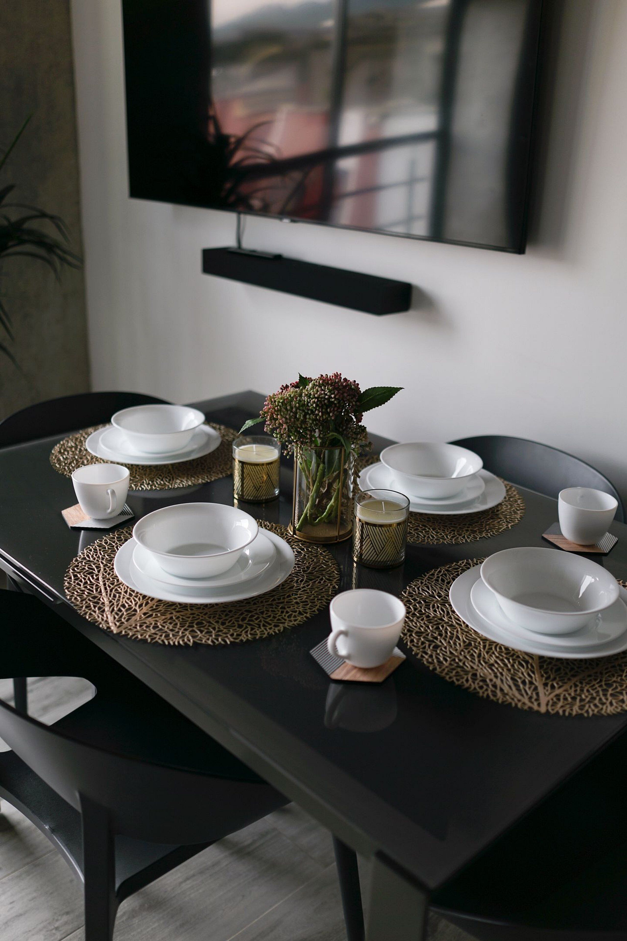 A dining table set with white plates, bowls, and cups, accompanied by a vase of flowers and candles.