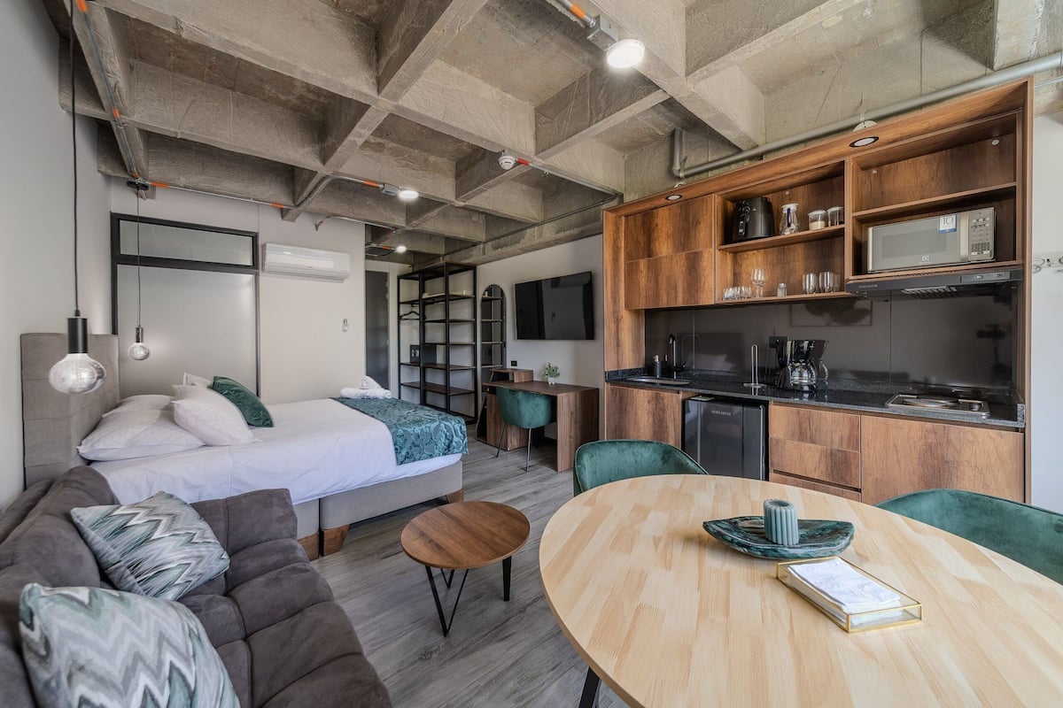 Ein modernes, kompakter Wohnraum mit Bett, Sofa, Esstisch, Küchenzeile und kleinem Arbeitsplatz.