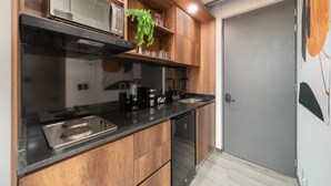 A modern kitchen with wooden cabinets, a black countertop, a built-in microwave, and a coffee machine. - Epic Suites x Ahead (Pereira)