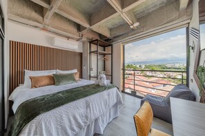 Ein modernes Schlafzimmer mit einem großen Bett, Blick auf die Stadt und einem Balkon mit Geländer.