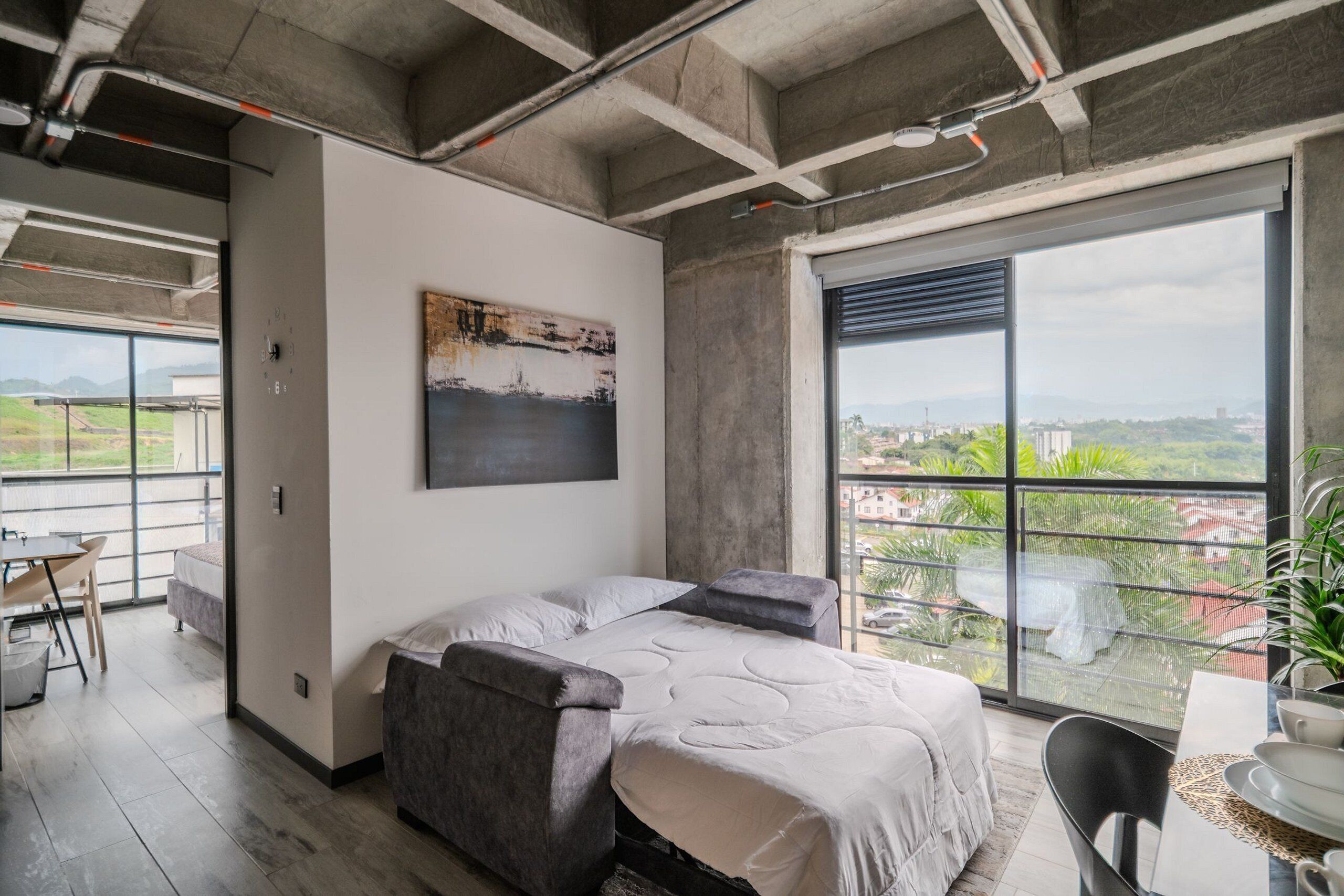Ein modernes Schlafzimmer mit großem Bett, Stadtblick und Balkon mit Tisch und Stühlen.