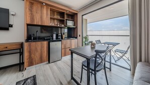 A modern kitchen with wooden cabinets and a built-in oven, a dining area with a table and chairs, and a balcony with a view of the sky. - Epic Suites x Ahead (Pereira)