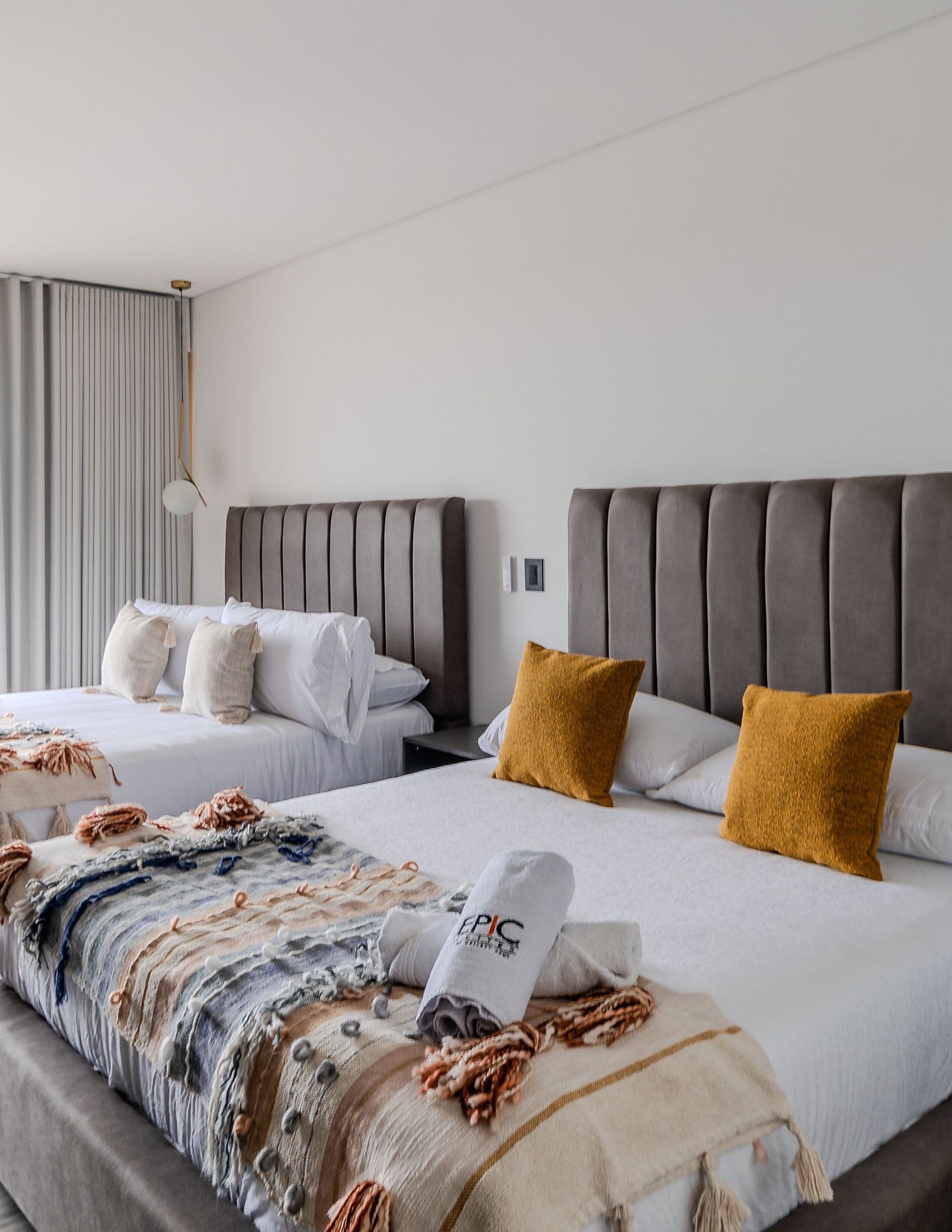 Ein Hotelzimmer mit zwei Betten, einem großen Fenster mit Vorhängen und einer modernen Lampe.