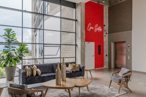 Eine moderne Lobby mit einem großen Fenster, einer roten Akzentwand, einer Couch mit Kissen und einem Couchtisch.