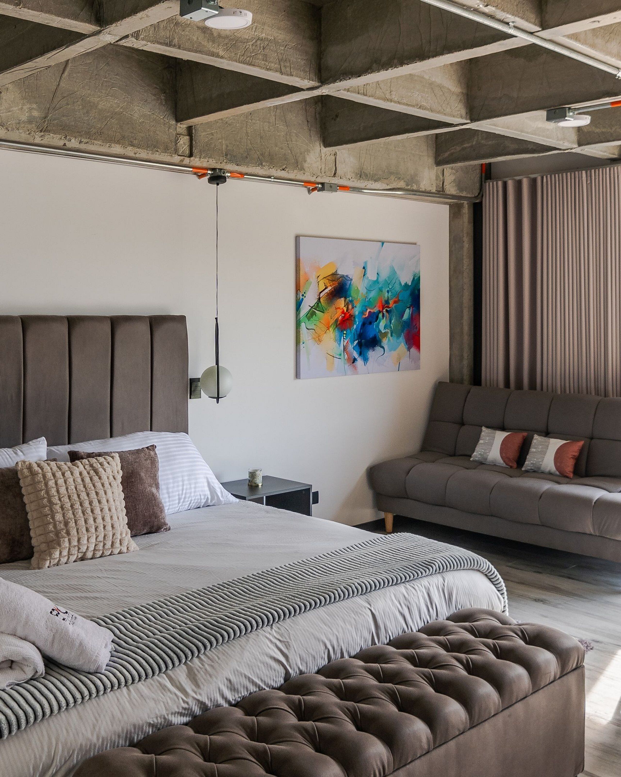 Ein modernes Schlafzimmer mit einem großen Bett, einer Couch und einem farbenfrohen abstrakten Gemälde.