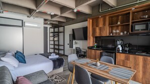 A compact hotel room with a bed, sofa, dining table, and kitchenette. - Epic Suites x Ahead (Pereira)
