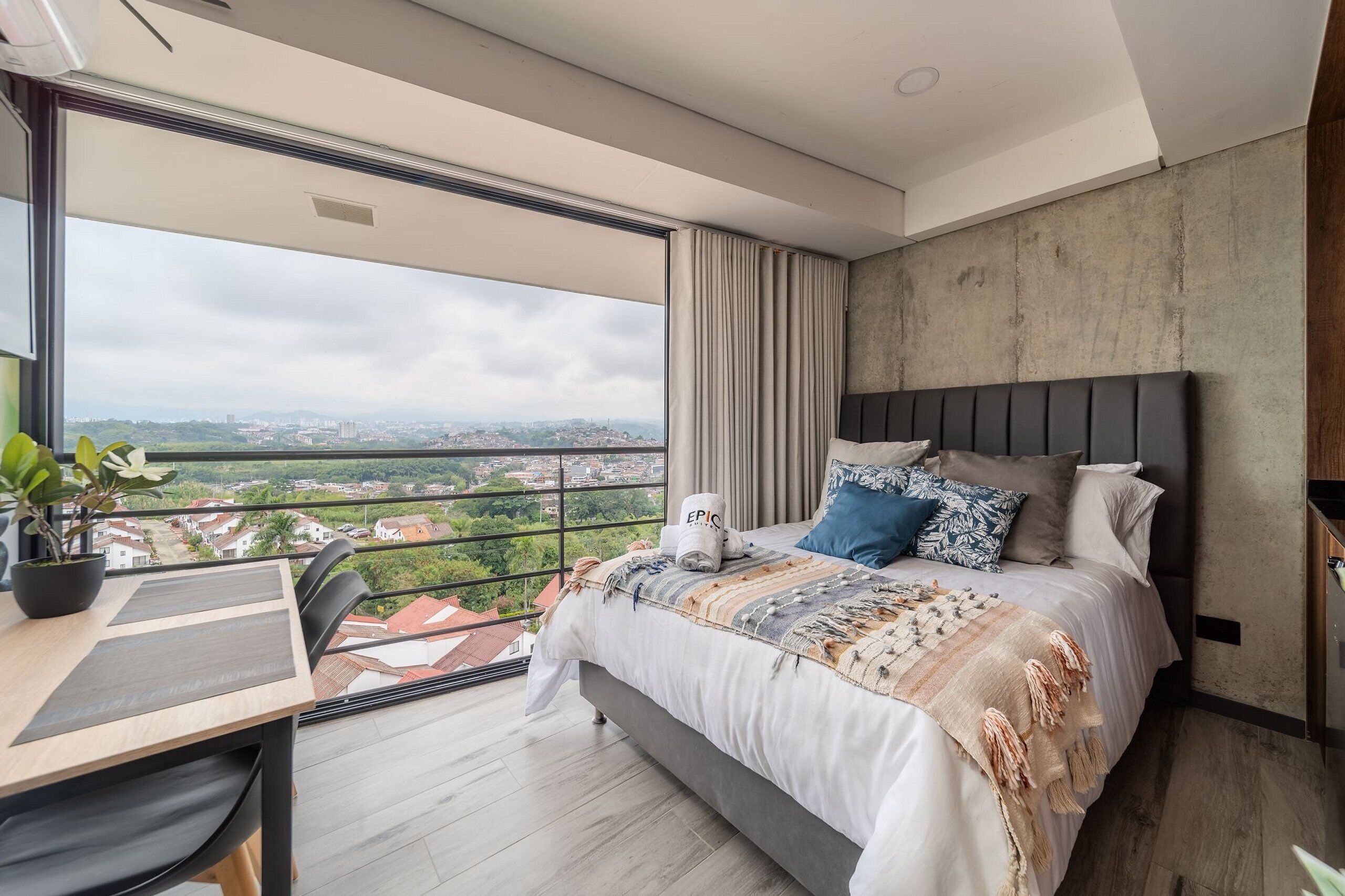 Ein modernes Schlafzimmer mit einem großen Bett, einem Schreibtisch und einem Balkon mit Blick auf die Stadt.