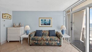 A living room with a floral sofa, two side tables with lamps, a dresser, a framed picture on the wall, and a sliding glass door leading to a balcony. - Atlantica 903, Oceanfront Stay, Myrtle Beach Rental (Myrtle Beach)